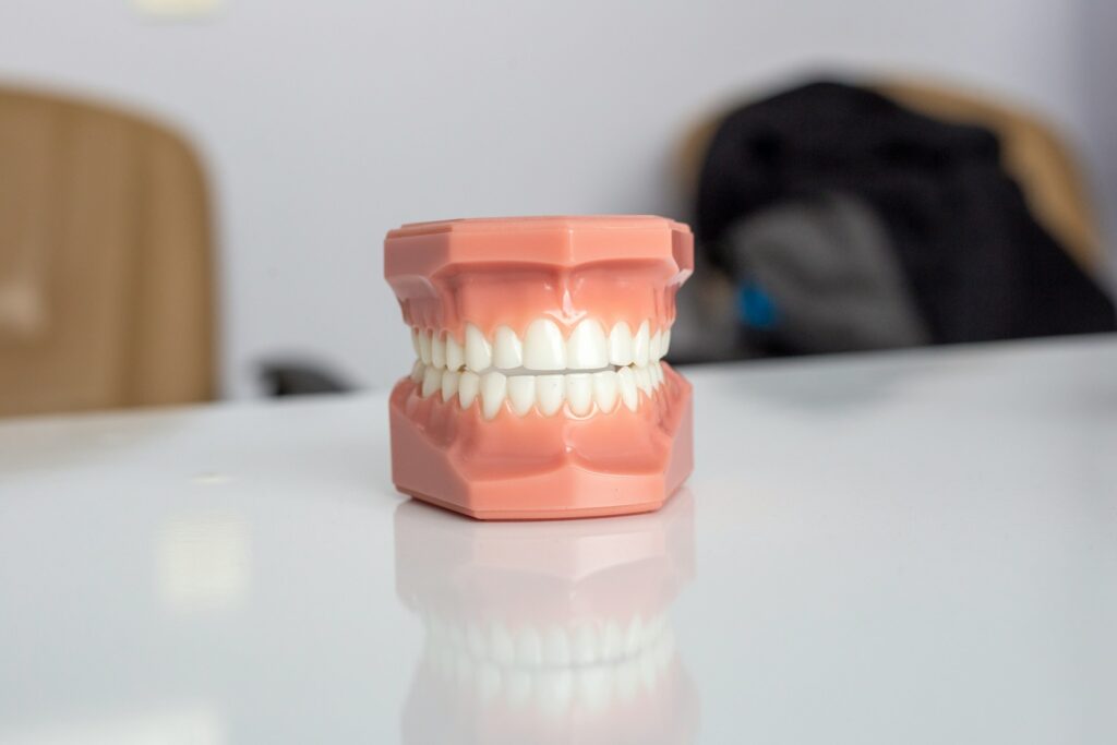 Pink dental typodont model showing a full set of straight white teeth on a glossy clinic table, illustrating porcelain veneer results