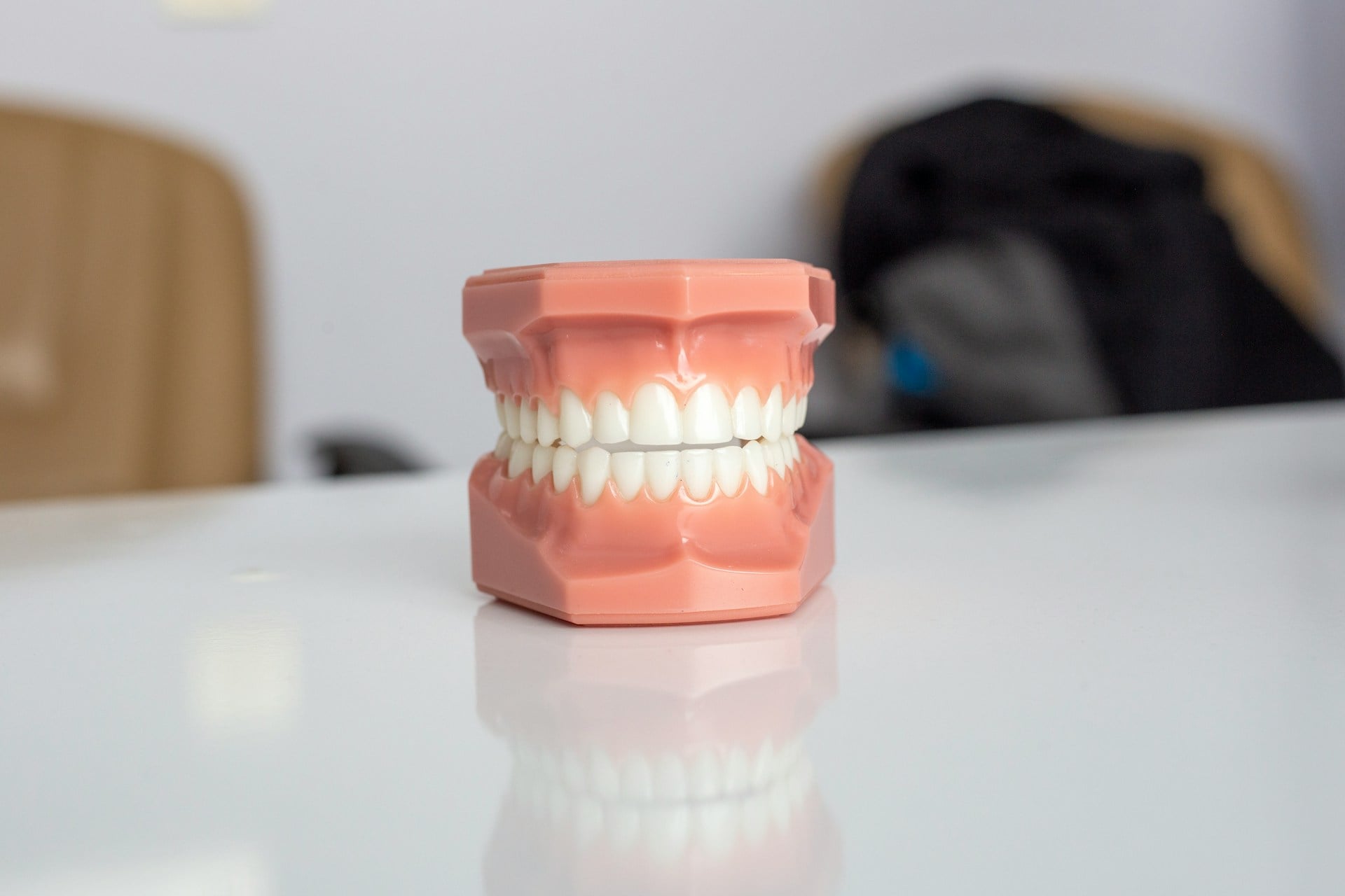 Pink dental typodont model showing a full set of straight white teeth on a glossy clinic table, illustrating porcelain veneer results